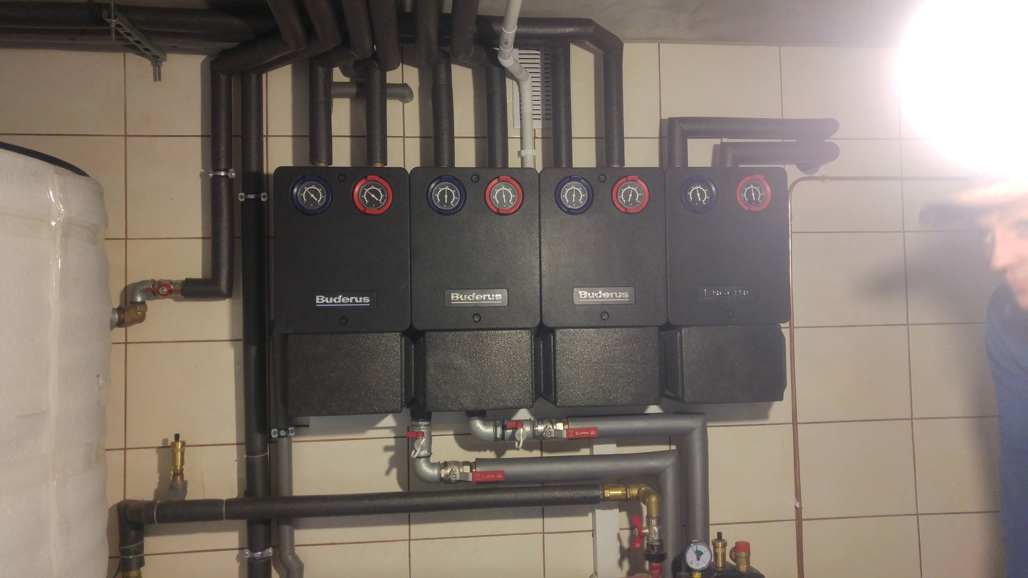 Cztery kotły grzewcze Buderus zamontowane na ścianie z beżowych płytek w Nowym Targu, widoczne rury instalacji grzewczej z izolacją.