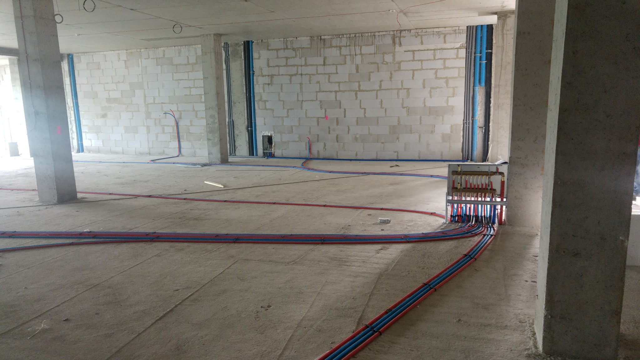 Rozprowadzenie rur instalacji centralnego ogrzewania i wodnej w surowym stanie deweloperskim, widoczny rozdzielacz i piony w ścianach z betonu komórkowego.