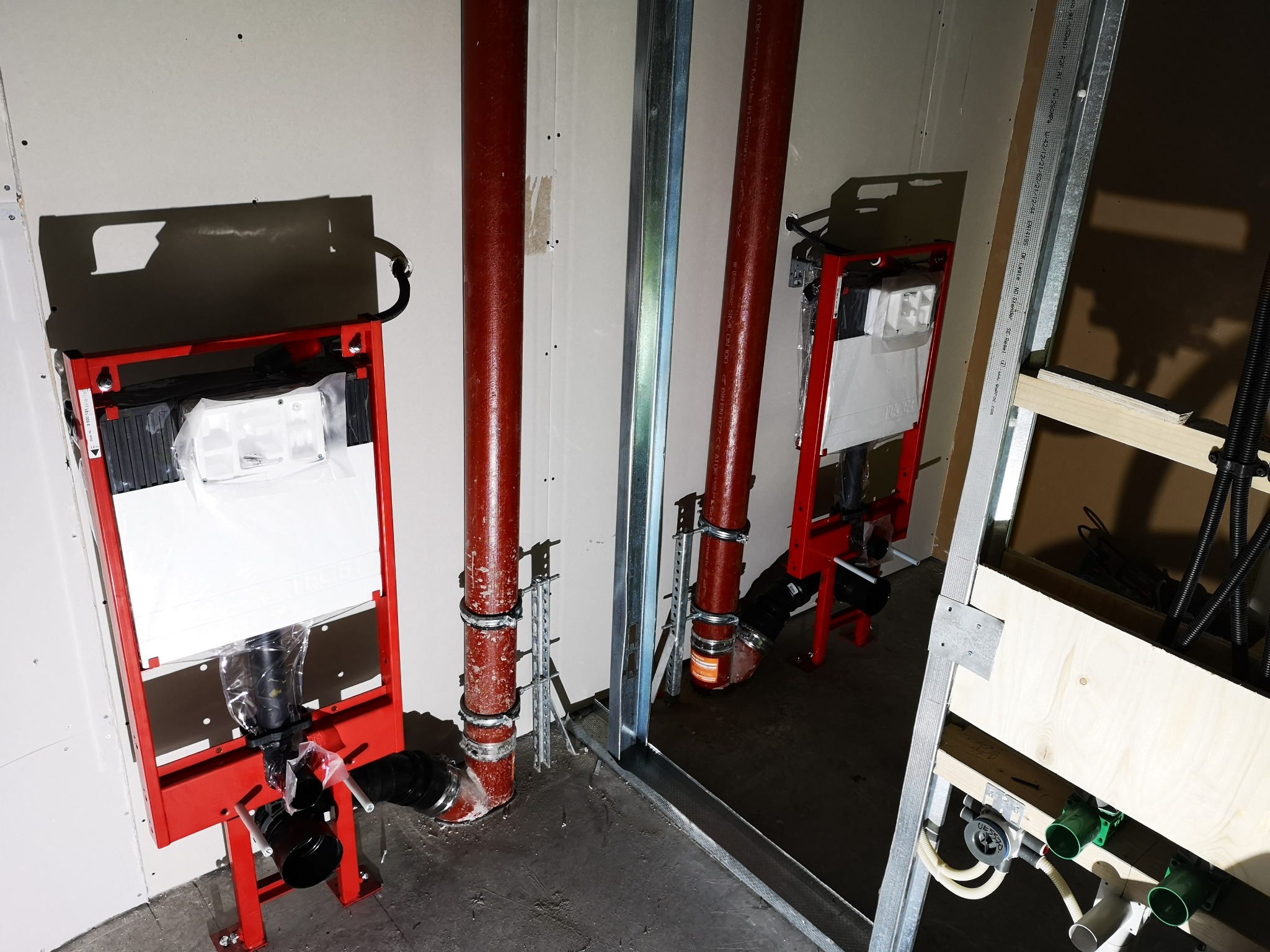 Stelaże podtynkowe WC zamontowane w surowym stanie, widoczne rury kanalizacyjne i elementy konstrukcyjne ścian działowych z profili stalowych.