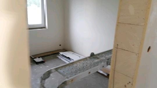 Wnętrze pokoju w trakcie remontu, widoczny aluminiowy podest roboczy, okno, przygotowane płyty gipsowe i narzędzia malarskie.