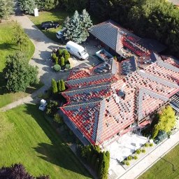 Hek-Deker Ciesielstwo -Dekarstwo Krzysztof Niciejewski - Widok z lotu ptaka na wielospadowy dach domu w trakcie wymiany pokrycia, widoczne fragmenty starego pokrycia, nowa więźba, samochód dostawczy i kontener na odpady na posesji.