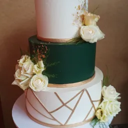Trzypiętrowy tort w odcieniach bieli i zieleni, zdobiony złotem i białymi różami, ustawiony na białym podeście.