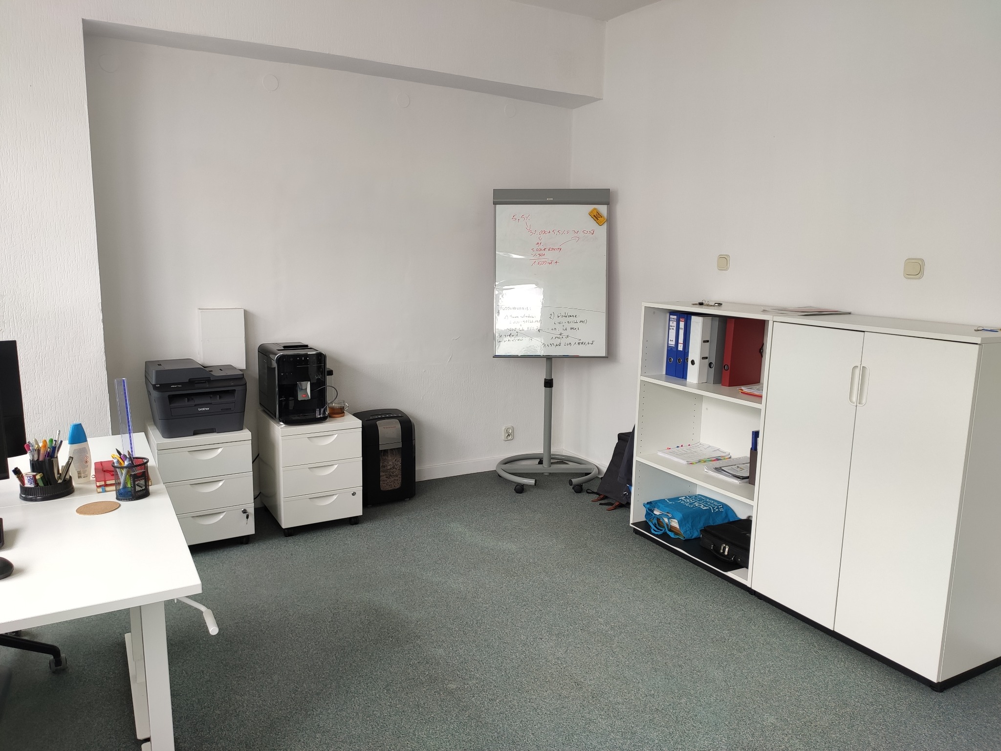 Jasne biuro z białymi meblami, biurkiem z akcesoriami biurowymi, drukarką, niszczarką i tablicą suchościeralną z zapiskami.