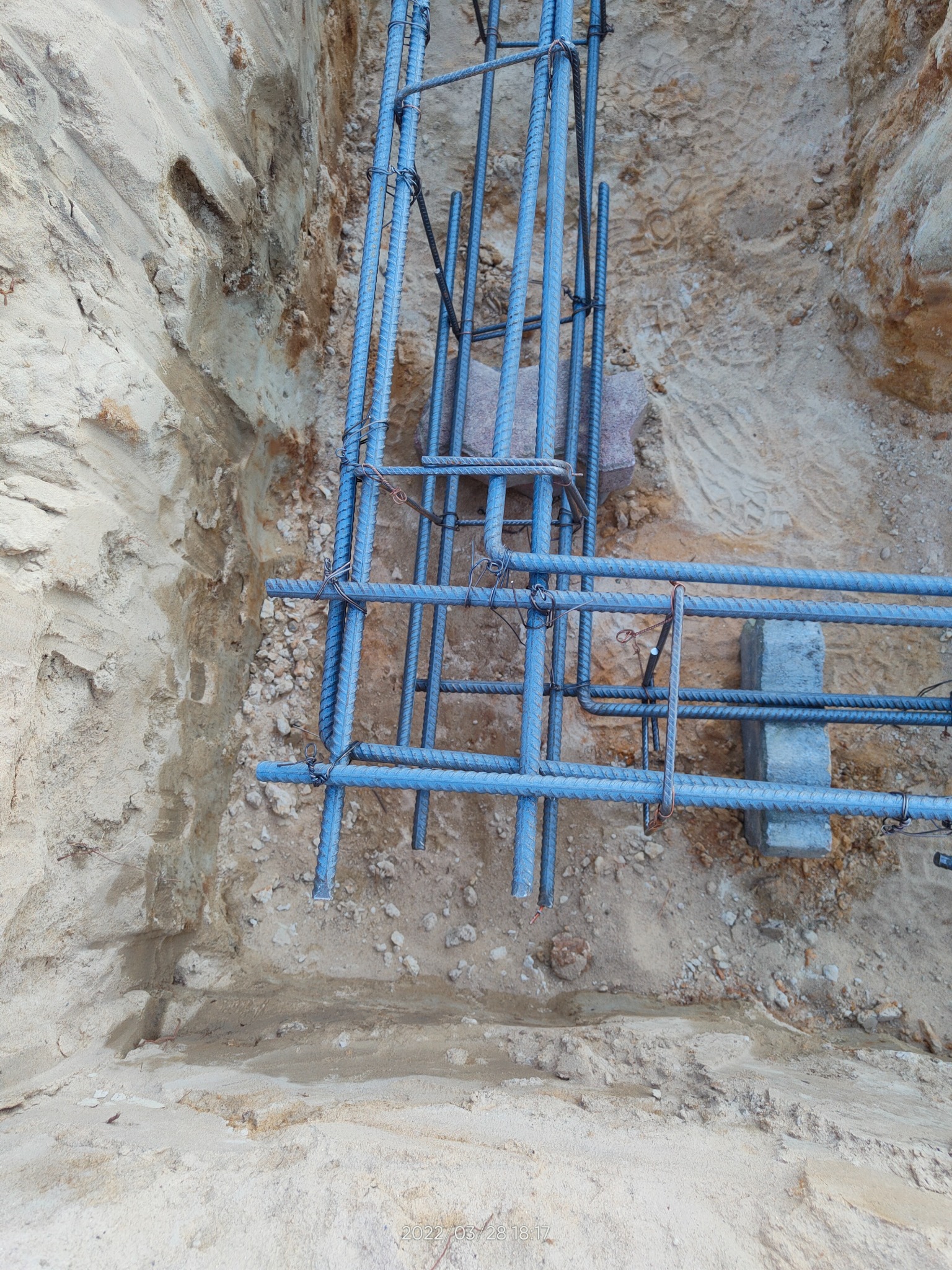 Zbrojenie fundamentu z prętów stalowych, zbrojenie powiązane drutem, umieszczone w wykopie z piaskową ziemią, widok z góry.