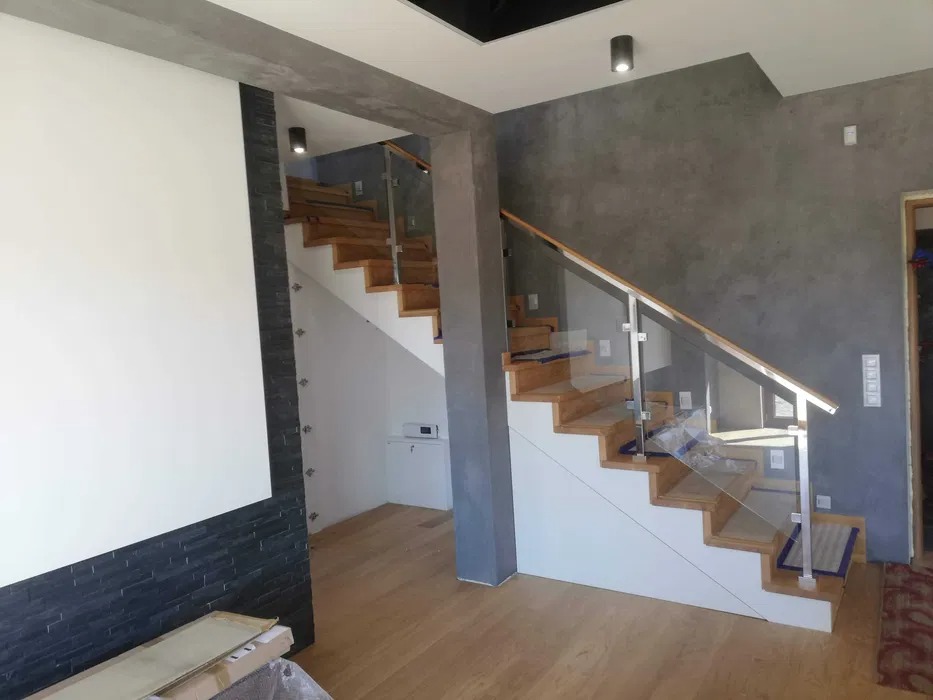 Nowoczesne drewniane schody z przezroczystą szklaną balustradą i metalowymi słupkami, widoczne z poziomu podłogi.