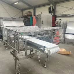 Konstrukcja ze stali nierdzewnej z siatką i taśmociągiem w hali produkcyjnej, widoczne elementy sterujące i inne maszyny w tle.