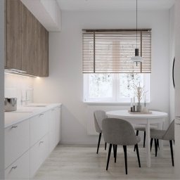 Home by M Martyna Matuszak - Jasna kuchnia z drewnianymi akcentami w Zielonej Górze: minimalistyczne szafki, okrągły stół z szarymi krzesłami i widok na zimowy krajobraz za oknem z żaluzjami.