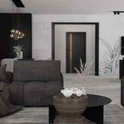 Home by M Martyna Matuszak - Nowoczesny salon w odcieniach szarości i czerni, z elementami dekoracyjnymi, takimi jak lampa wisząca z kulistymi kloszami, grafika roślinna na ścianie i drewniany stolik kawowy z filiżankami.