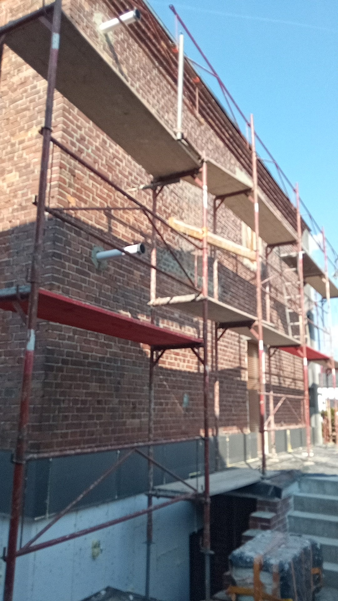 Ceglana elewacja budynku w trakcie prac, widoczne rusztowania, fragment ocieplenia i rura wentylacyjna wystająca ze ściany w Piekary.
