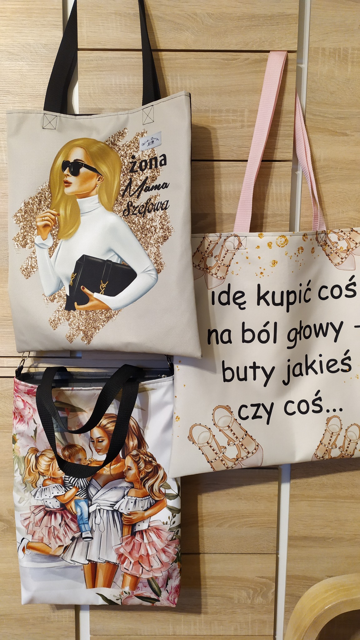 Trzy płócienne torby na zakupy z różnymi nadrukami: blondynka z torebką, napis 'Idę kupić coś na ból głowy - buty jakieś czy coś...' z rysunkami butów, oraz matka z dziećmi w sukienkach.