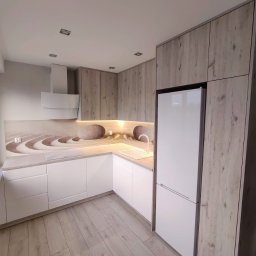 MEBLEKO - Jasna kuchnia z białymi frontami i drewnopodobnymi szafkami górnymi, blat z motywem zen, biała lodówka i podłoga w odcieniach szarości.