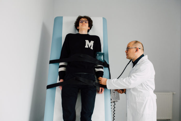 Pacjent leżący na stole podczas badania testem pochyleniowym (TILT test), lekarz osłuchuje serce stetoskopem.