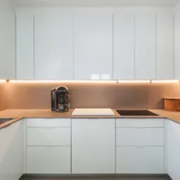 Nowoczesna, minimalistyczna kuchnia z białymi, lakierowanymi frontami, podświetleniem LED pod szafkami wiszącymi i sprzętem AGD w zabudowie.