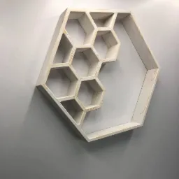 Półka ścienna w kształcie plastra miodu, wykonana z bielonego drewna, zamontowana na szarej ścianie, rzucająca cień.