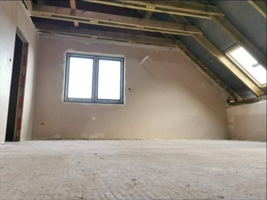 Poddasze po nałożeniu gładzi gipsowej, widoczne okno dachowe i okno fasadowe, surowe drewniane elementy konstrukcyjne dachu