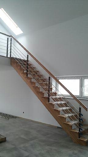 Drewniane schody z balustradą ze stali nierdzewnej w nowoczesnym domu, widok z dołu, surowe wykończenie podłogi.