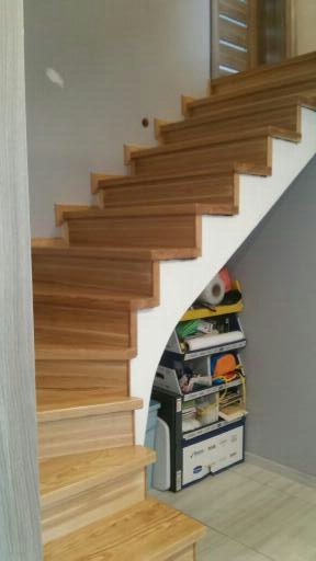 Jasne, drewniane schody z białymi podstopnicami, z półkami schowanymi pod biegiem schodów, widoczne akcesoria i narzędzia.