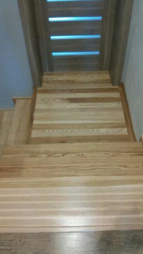 Nowoczesne schody drewniane z jasnego drewna prowadzące do drzwi z przeszkleniami w poziomych pasach, widok z góry.