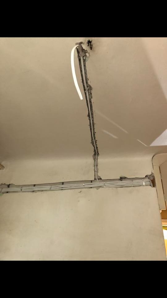 Wykuta bruzda w suficie i ścianie z poprowadzonymi przewodami elektrycznymi w białej rurce instalacyjnej, częściowo zamaskowana gipsem.