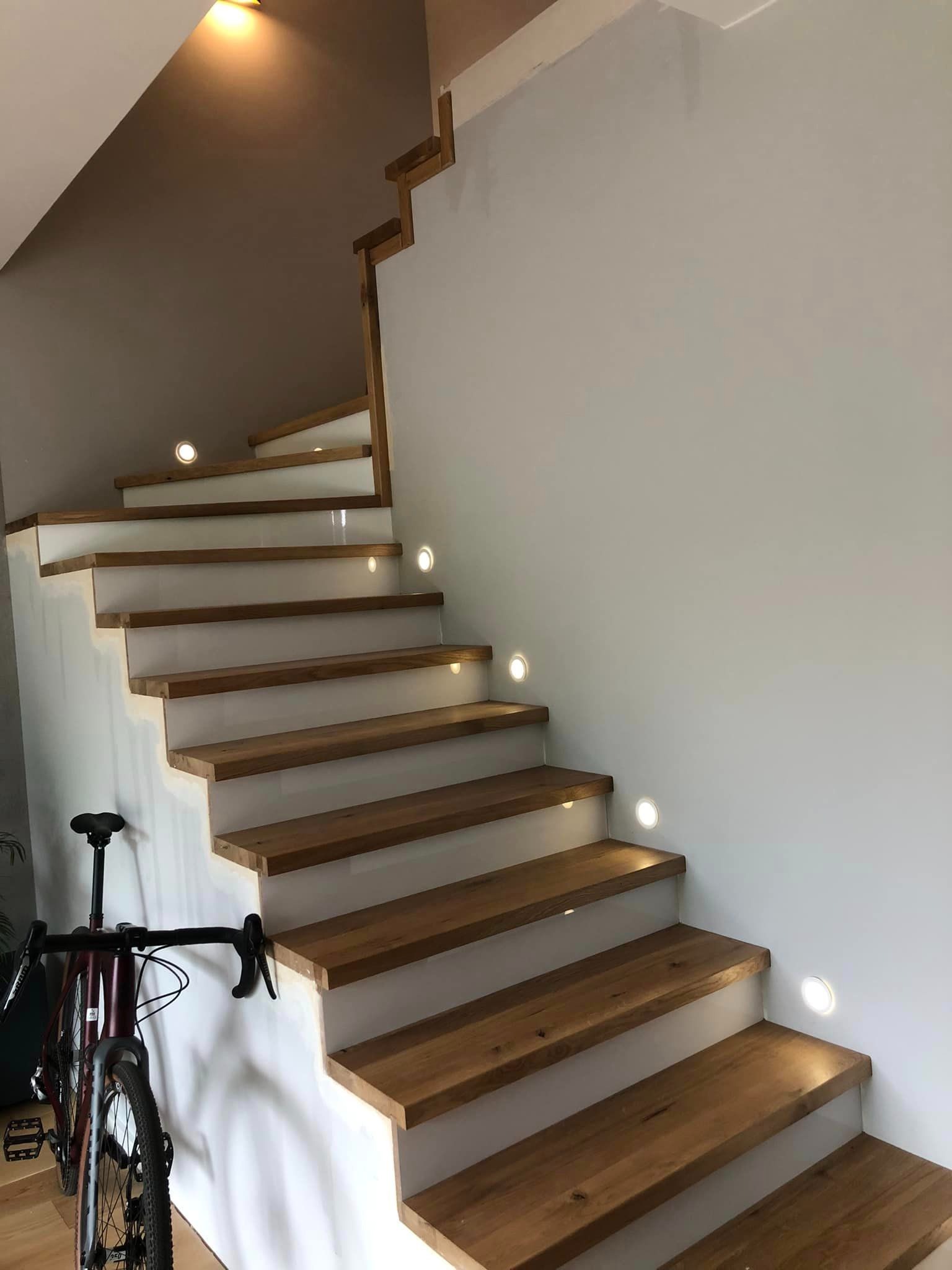 Drewniane schody z podświetleniem LED w ścianie, zamontowane w domu w Warszawie, obok stoi rower.