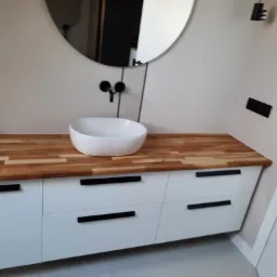 Nowoczesna łazienka: biała szafka z drewnianym blatem, okrągłe lustro i czarna armatura, minimalistyczny design.