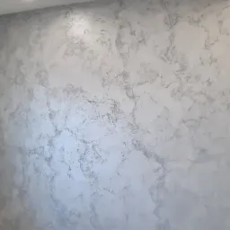 Ściana wykończona dekoracyjną szpachlą w odcieniach szarości, imitująca marmur, z zamontowanymi gniazdkami elektrycznymi i antenowym.