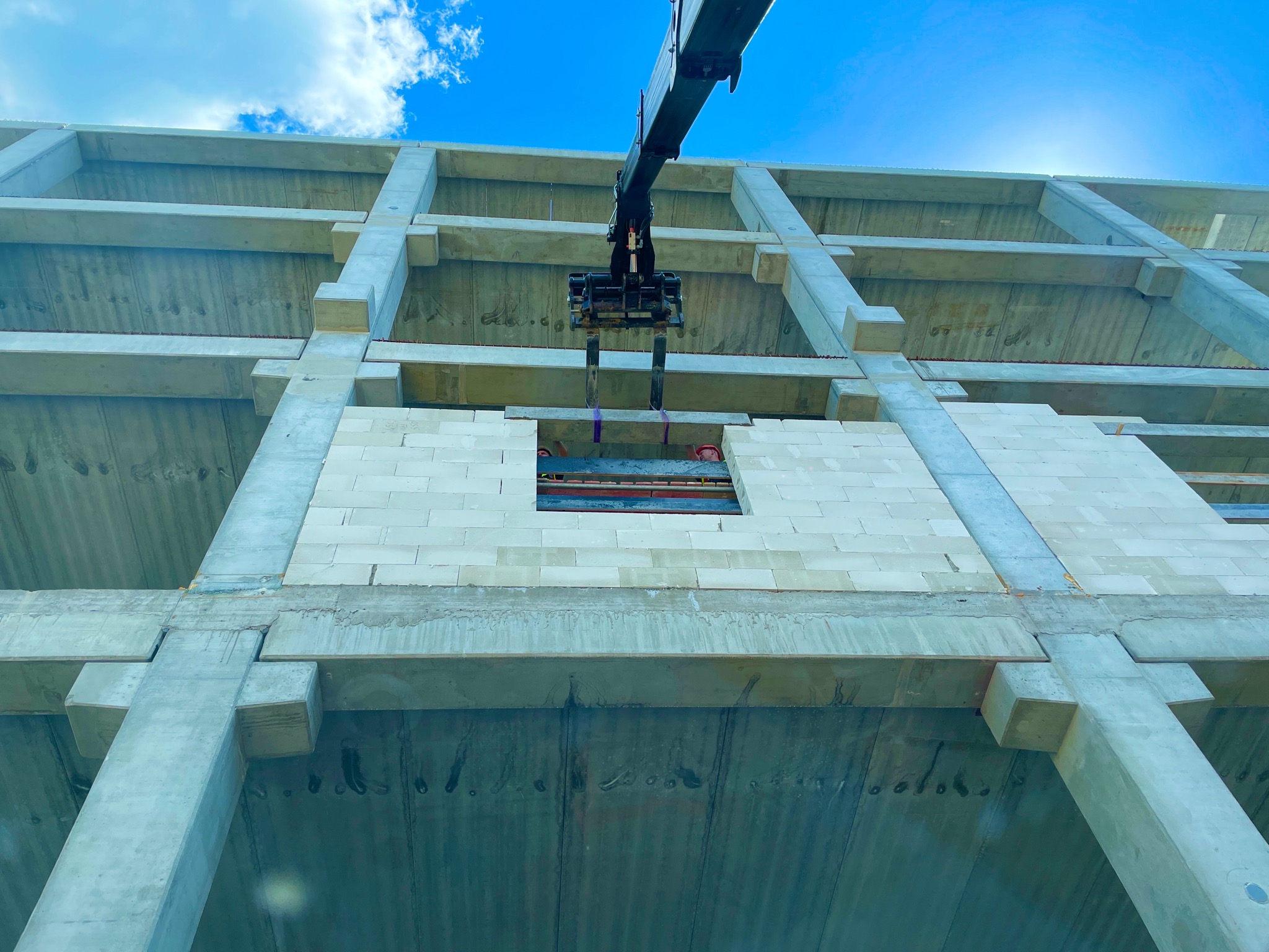 Wznoszenie surowej konstrukcji budynku wielopiętrowego z betonu i bloczków, widok z dołu na pracę żurawia przenoszącego materiały na wyższe kondygnacje.