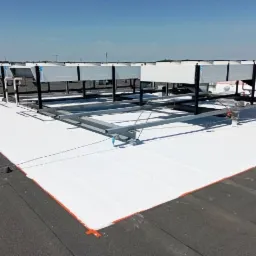 Biała, gładka izolacja termiczna dachu płaskiego z widocznymi elementami mocującymi i systemem klimatyzacji na konstrukcji stalowej.