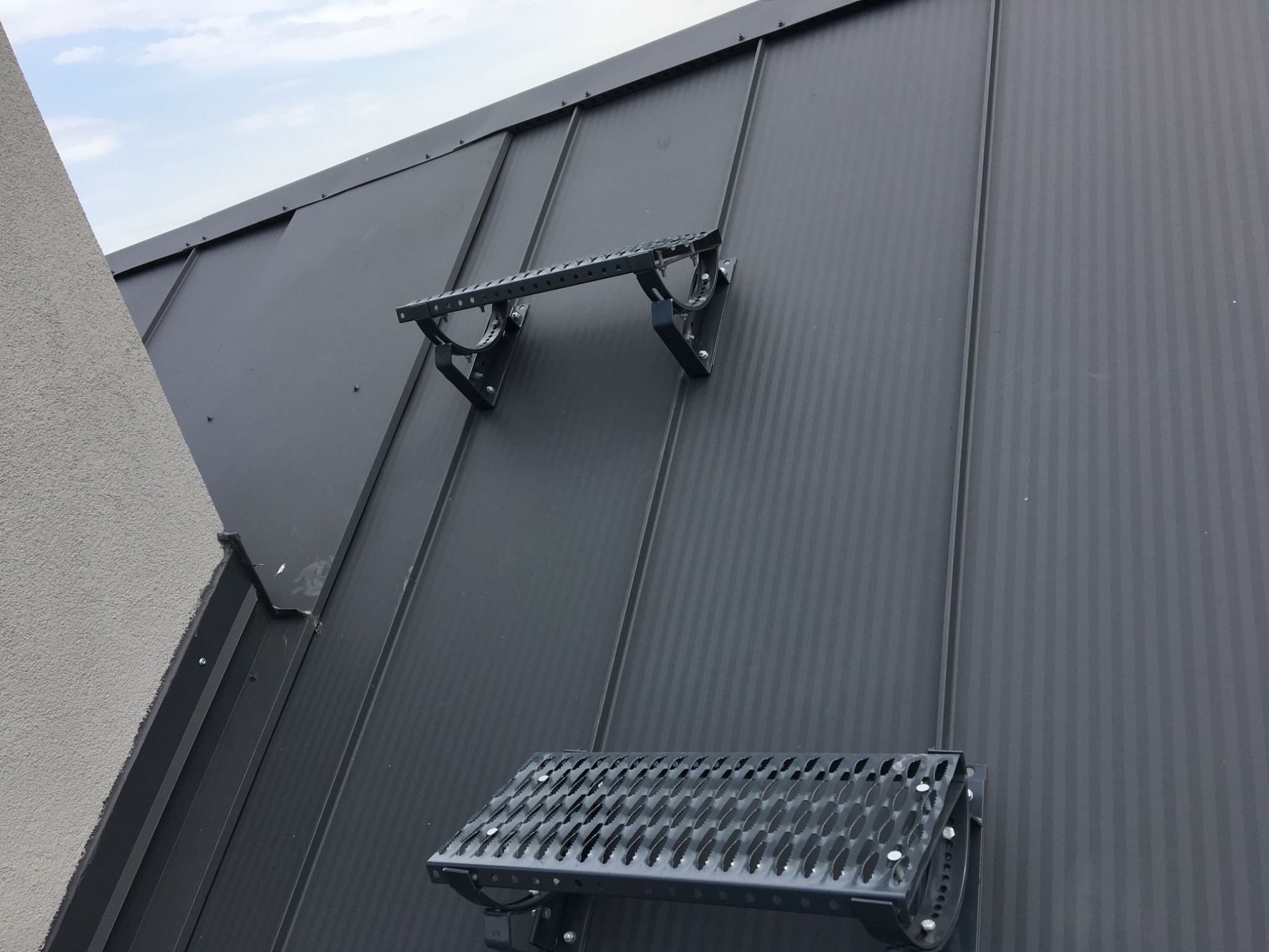 Ciemnoszary dach z blachy trapezowej z zamontowanymi metalowymi stopniami dachowymi w celu bezpiecznego poruszania się po połaci.