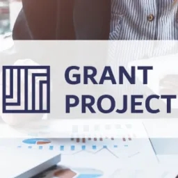 Kobieta w koszuli w paski trzyma tablet nad stołem z laptopem i wykresami kołowymi, logo Grant Project na pierwszym planie.