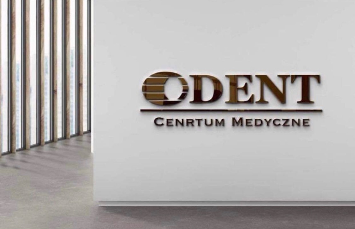 Metalowe litery z nazwą 'ODENT' i napisem 'CENTRUM MEDYCZNE' na białej ścianie w nowoczesnym wnętrzu, widok z boku.