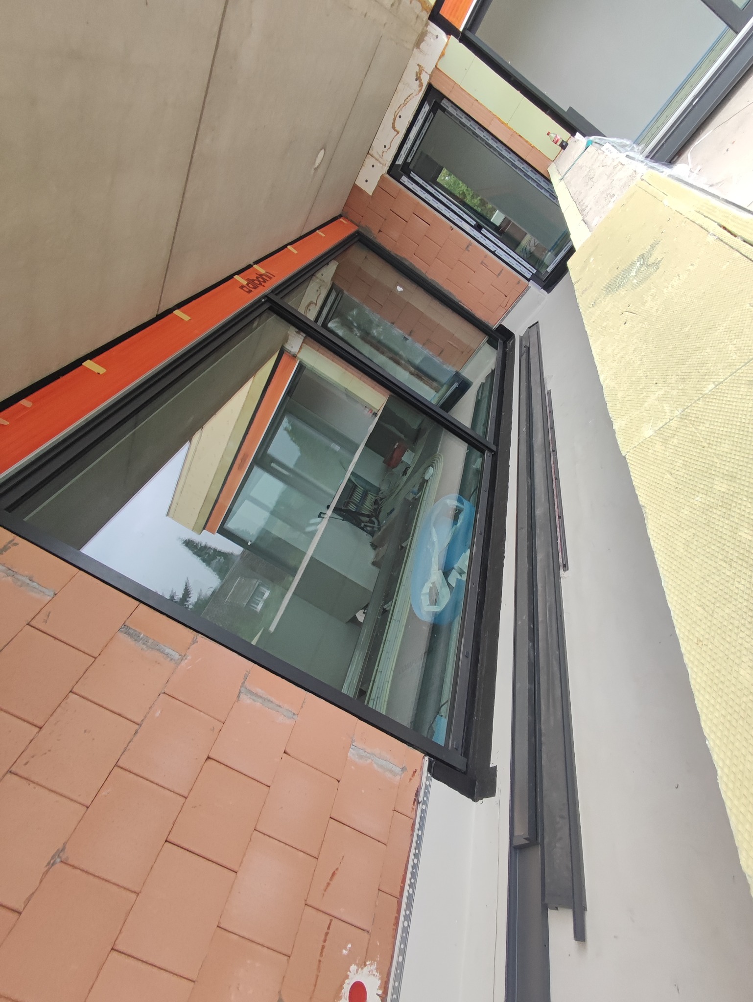 Montaż okien z czarnymi ramami w nowym budynku, widoczne cegły wokół okien i izolacja termiczna na ścianie.