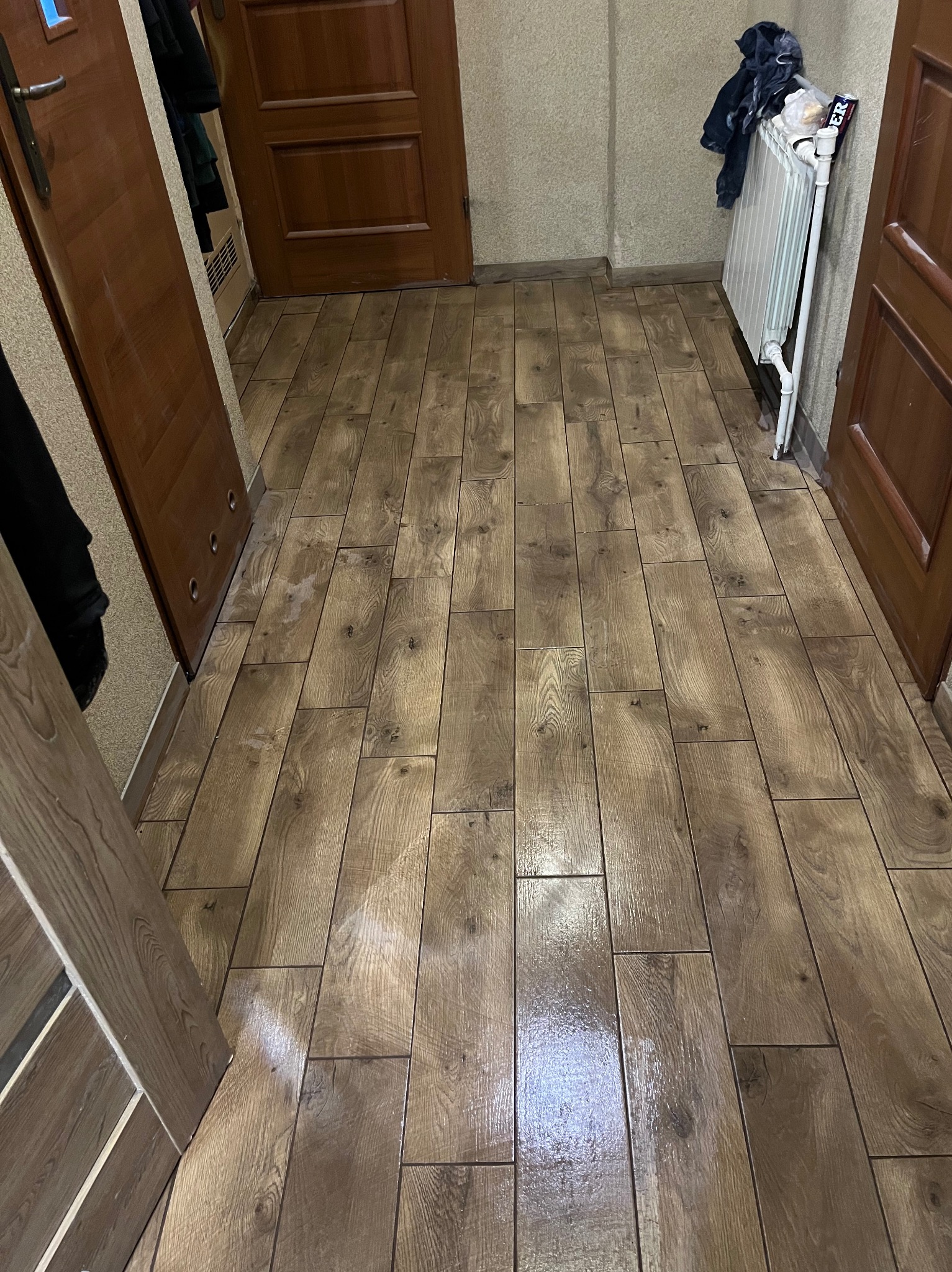 Ułożone panele podłogowe imitujące drewno w korytarzu z trzema drewnianymi drzwiami i białym grzejnikiem. Widok z góry, lekki połysk paneli.