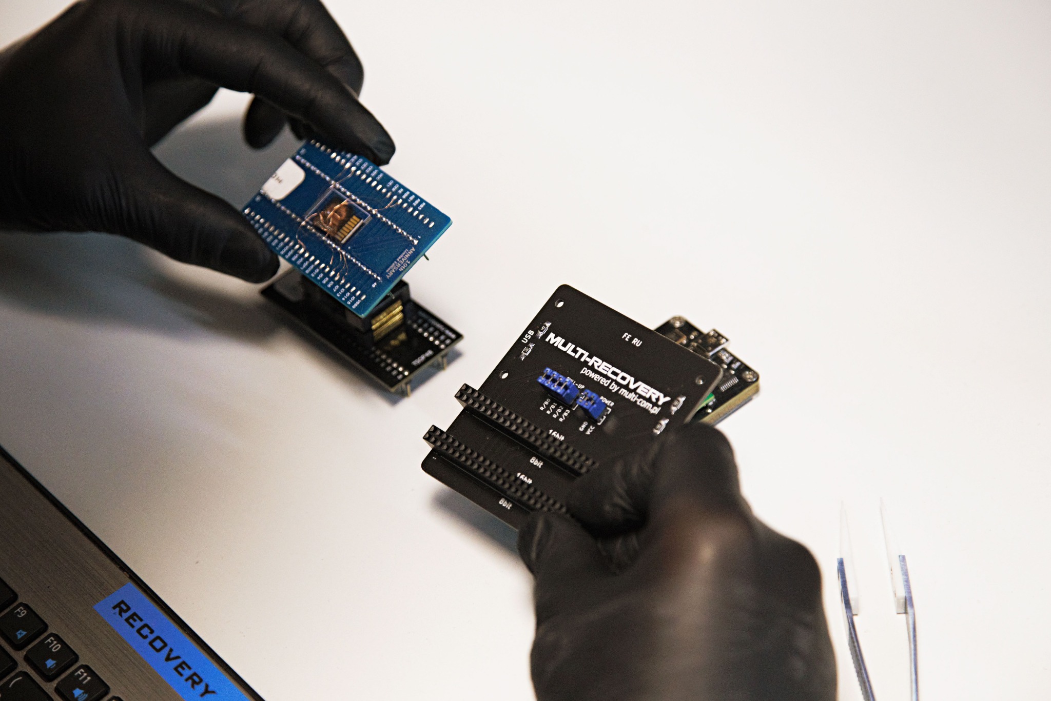 Odzyskiwanie danych w Krakowie: Inżynier w rękawicach manipuluje płytką Multi-Recovery, narzędzia i laptop z naklejką 'Recovery' na białym tle.