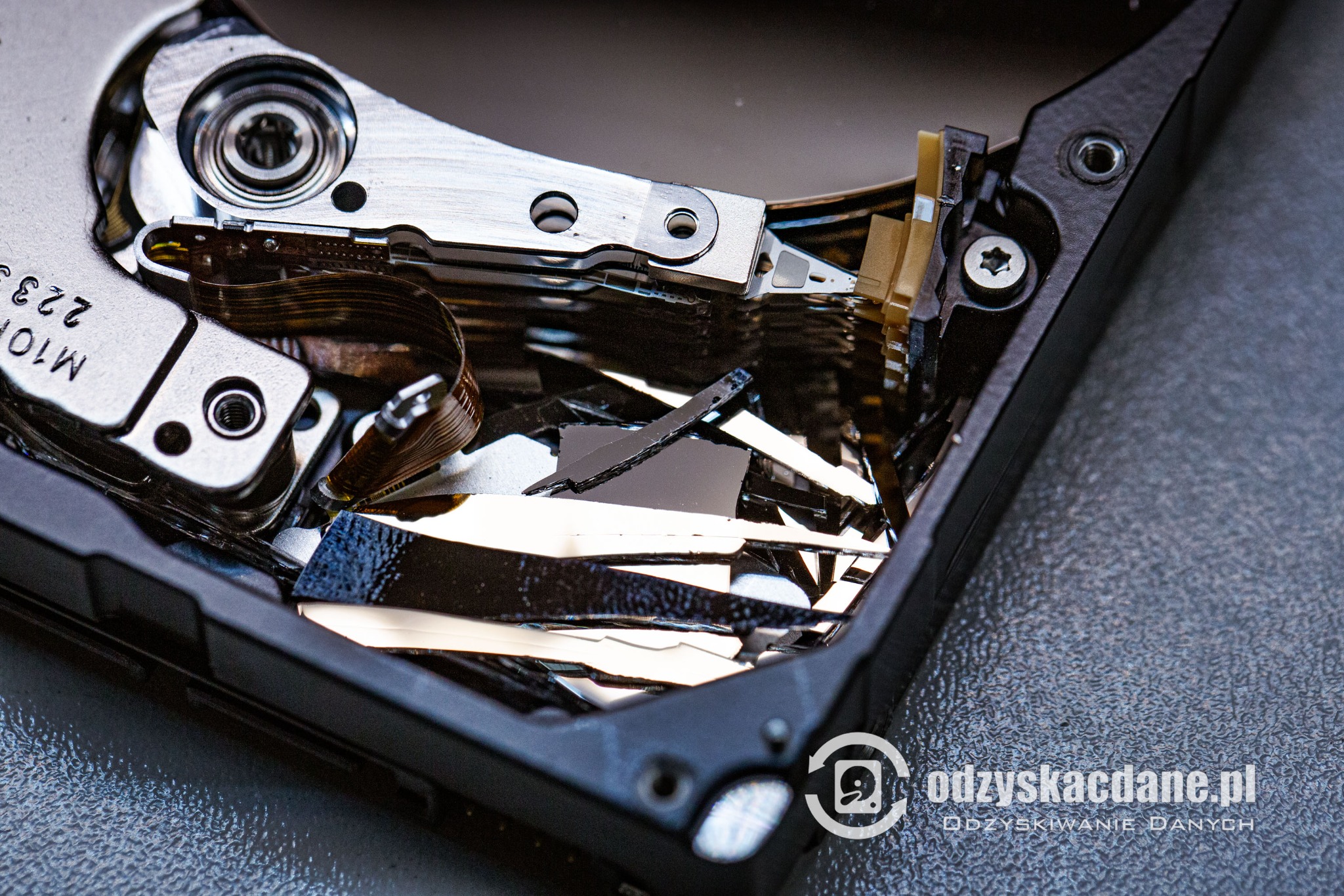 Otwarty dysk twardy z uszkodzonymi talerzami, widoczne elementy mechaniczne i fragmenty nośnika danych. Makro, ostre światło.