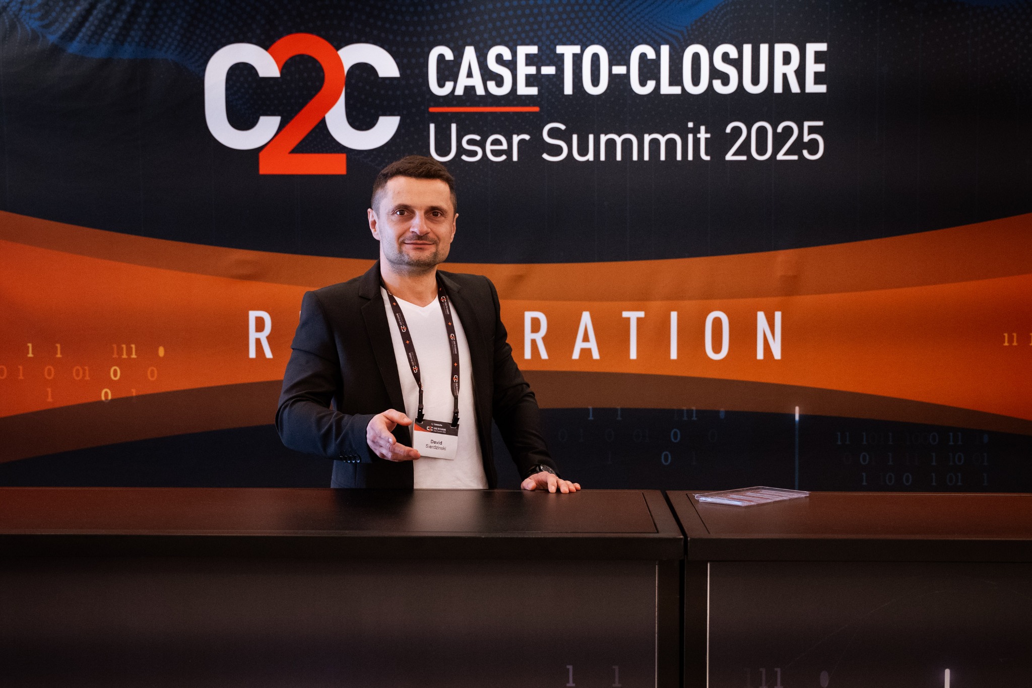 Technik na tle ściany z logo Cellebrite C2C User Summit 2025, z identyfikatorem David Sierdzinski, prezentuje zaplecze sprzętowe firmy Data Recovery.