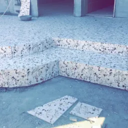 Wykończone płytkami lastryko schody zewnętrzne z dwoma stopniami, z widocznymi niedociągnięciami i płytkami do ułożenia na posadzce.