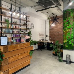 AKdecor - Studio projektowe - Nowoczesne wnętrze salonu kosmetycznego z drewnianą recepcją, półkami z kosmetykami, ścianą z cegły i zieloną ścianą z mchu.