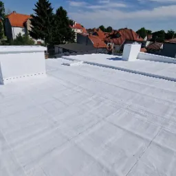 Biała, płaska powierzchnia dachu po hydroizolacji, z widocznymi kominami i otoczeniem zabudowy miejskiej w tle.