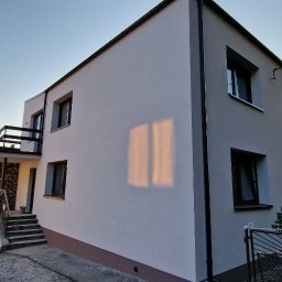 ARBAL SPÓŁKA Z OGRANICZONĄ ODPOWIEDZIALNOŚCIĄ - Dwupiętrowy dom z jasną elewacją i ciemnymi obramowaniami okien, widok z boku, z fragmentem ogrodzenia i zaparkowanym samochodem dostawczym.