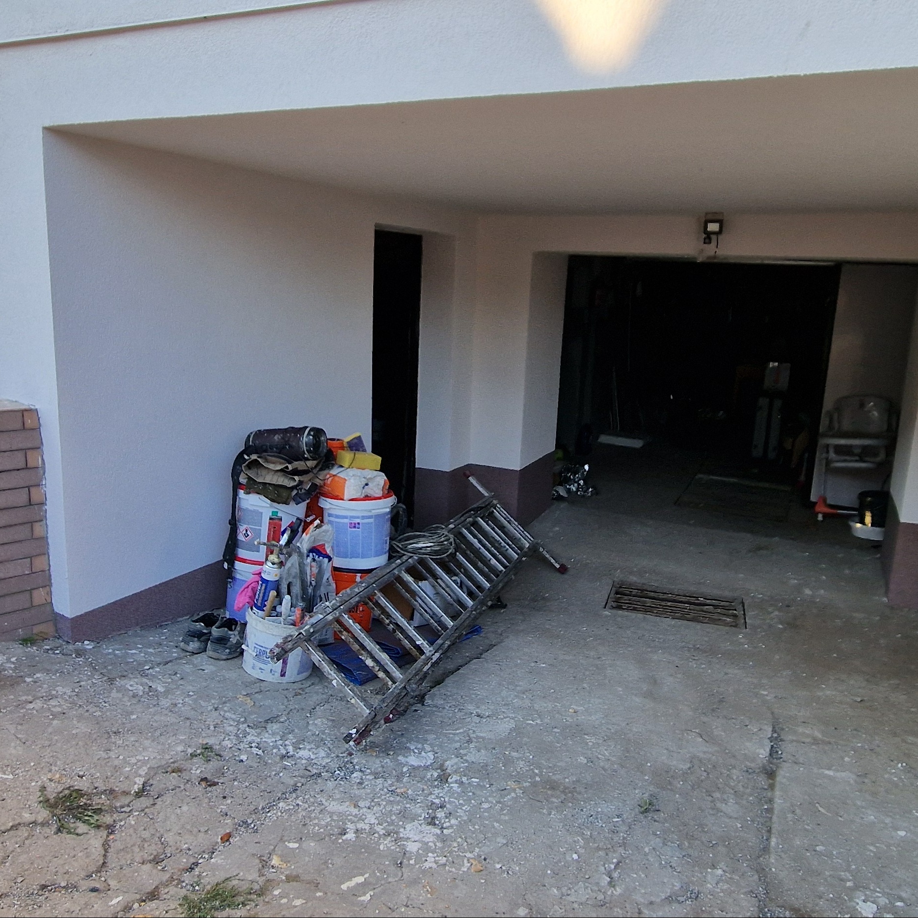 Stos wiader z farbą, pędzle i drabina oparta o świeżo pomalowaną elewację w prześwicie garażu