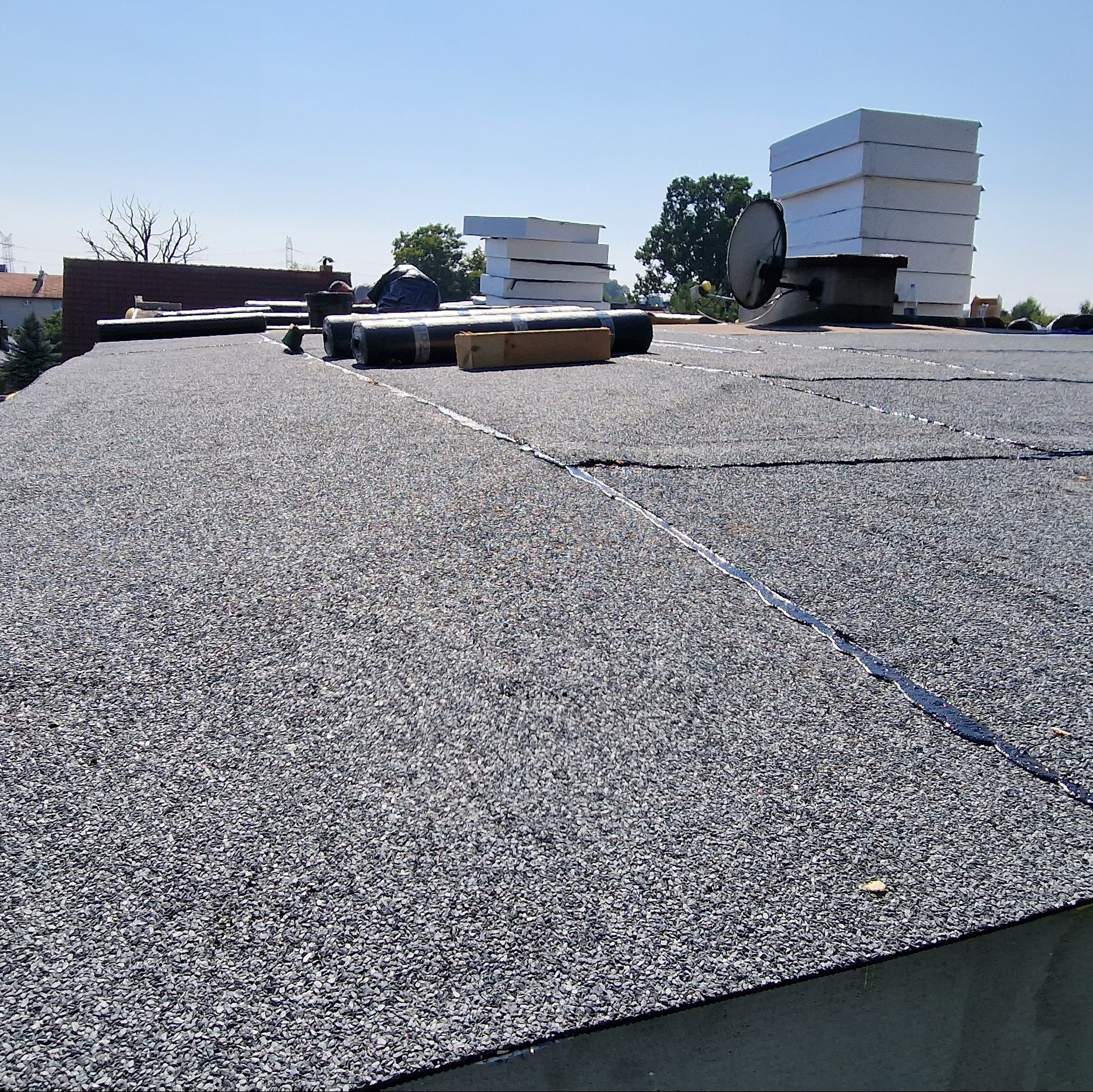 Wykończony dach pokryty papą z widocznymi zgrzewami i rolkami papy oraz izolacją termiczną w tle.