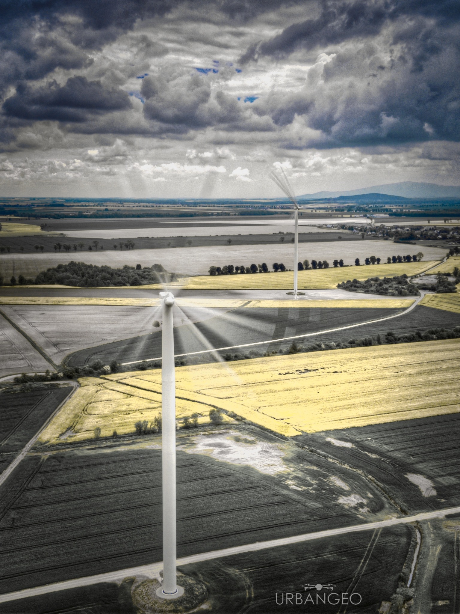 Dwa wiatraki na polach uprawnych pod pochmurnym niebem, widok z lotu ptaka z efektem kolorystycznym.