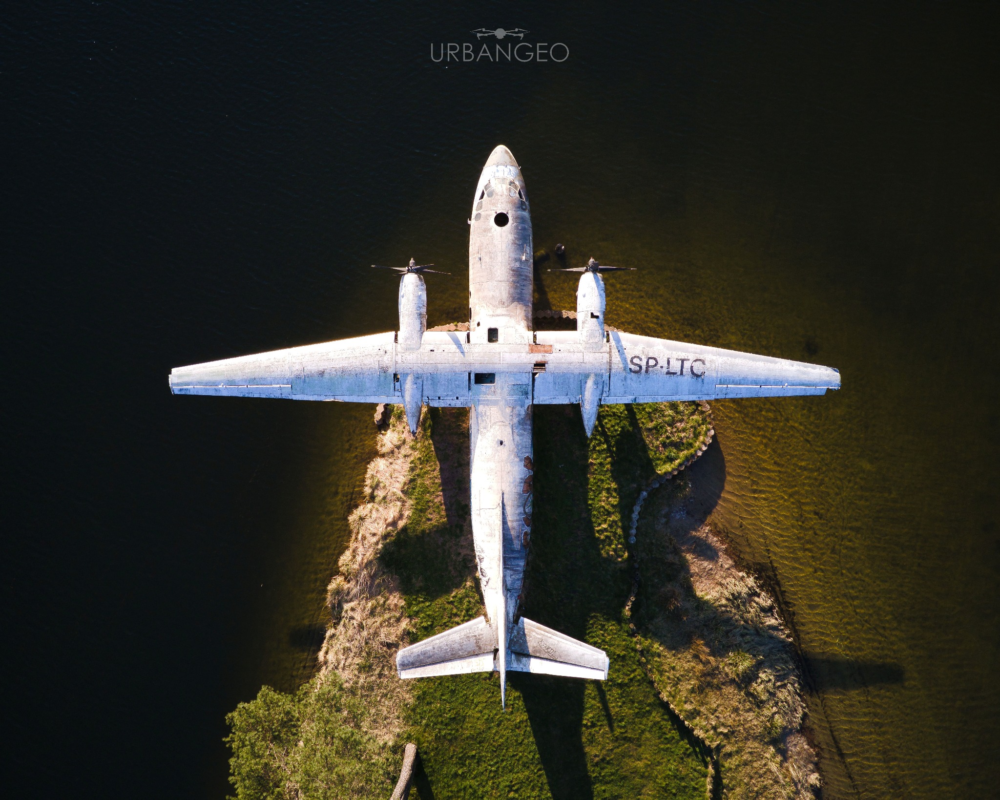 Zardzewiały samolot SP-LTC na brzegu jeziora, widok z drona, woda odbija promienie słońca.