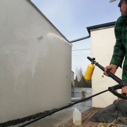 Dominik - Czyszczenie elewacji domu w Chełmży za pomocą myjki ciśnieniowej z żółtym pojemnikiem na detergent.