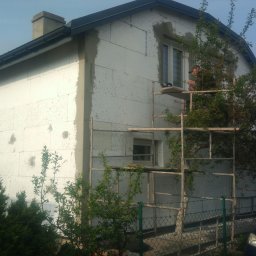 Dominik - Dom jednorodzinny w trakcie ocieplania styropianem, widoczne rusztowania i częściowo nałożona warstwa kleju, a także niezabezpieczone otwory na kołki.