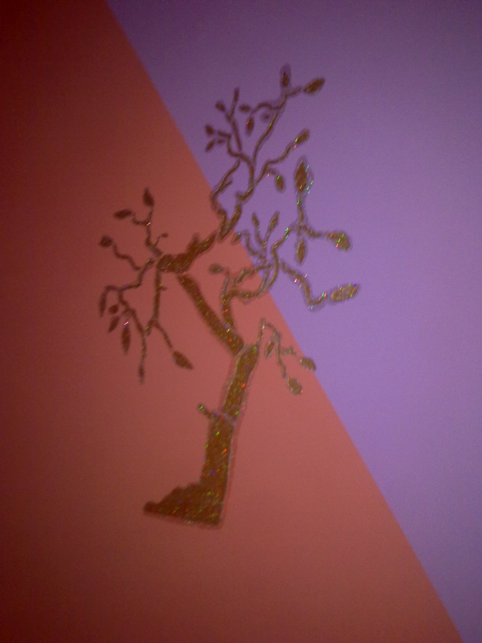 Błyszcząca naklejka drzewa na ścianie pomalowanej na różowo i fioletowo w układzie ukośnym.