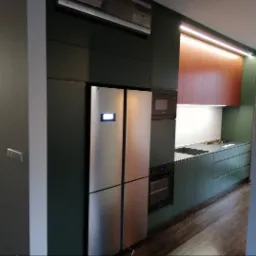 Nowoczesna kuchnia z zabudową w odcieniach zieleni i brązu, z lodówką side-by-side i oświetleniem LED podszafkowym, widok z boku.