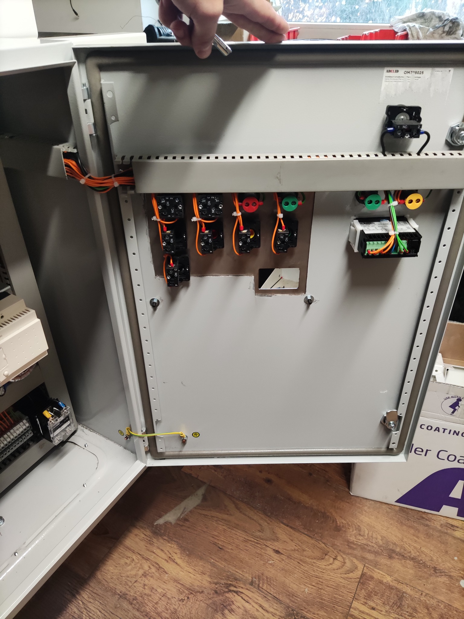 Otwarta szafa sterownicza z widocznymi elementami instalacji elektrycznej, w tym przekaźnikami, kostkami połączeniowymi i okablowaniem.