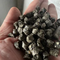 Garść ciemnych brykietów opału, widoczne pęknięcia i nierówna powierzchnia, na dłoni osoby.